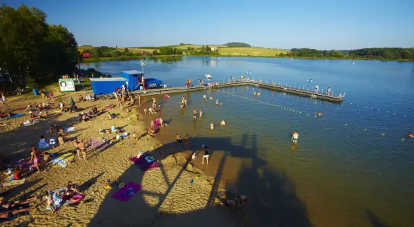 Słoneczny dzień nad zalewem w Siamoszycach. Ludzie odpoczywają na plaży i kąpią się w wodzie. Sprawdź cennik atrakcji!