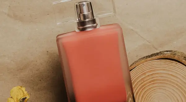 Perfumy Lancome Oui w koralowym odcieniu, obok suszonej róży i plastra drewna.