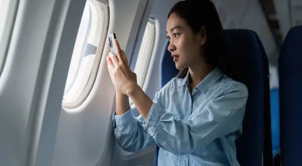 Kobieta w samolocie sprawdza telefon, zastanawiając się, czy w samolocie jest internet.