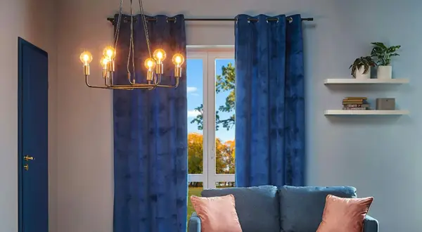 Elegancki, złoty żyrandol z żarówkami w stylu retro, wiszący nad kanapą, w salonie z granatowymi zasłonami.