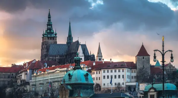 Prag dom mit seinen Türmen und Dächern unter dramatischem Himmel. Ein Vogel fliegt über die historische Kulisse.