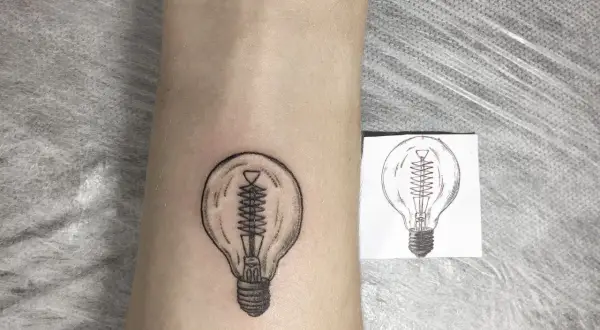 Nowy tatuaż żarówka na skórze, obok szkicu. Symbol pomysłu i światła.
