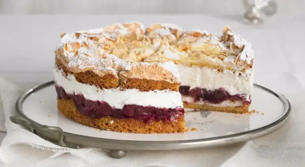 Eine köstliche Hansen Jensen Torte mit Kirschen, Sahne und Baiserhaube, bestreut mit Mandelblättchen und Puderzucker.