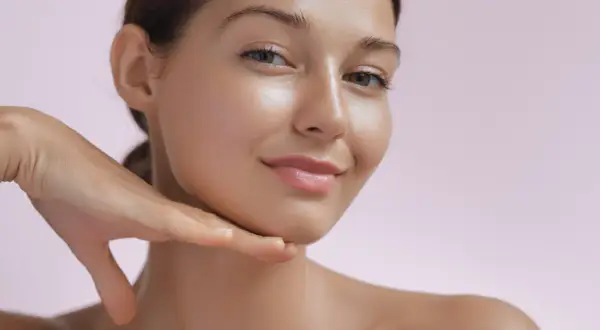 Strahlendes Gesicht einer Frau, die ihr Kinn berührt. Die Haut wirkt glatt und jugendlich, ein Zeichen für die positive retinol wirkung.