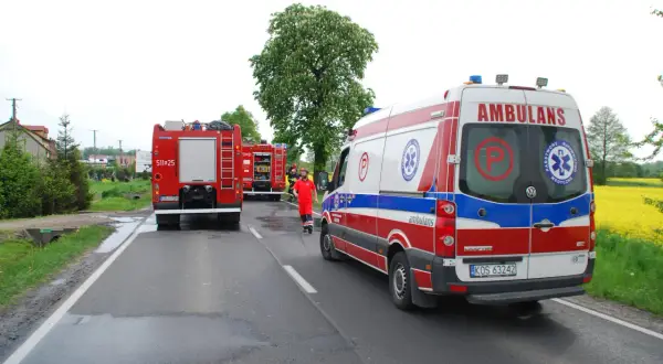Strażacki bosak leży na drodze obok wozu strażackiego i karetki pogotowia.