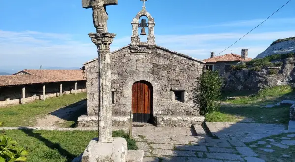 Crucero y ermita de piedra en el Castro de Santa Trega, bajo un cielo azul.