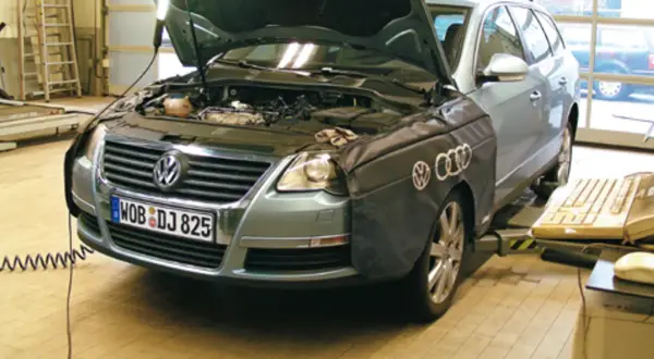 Passat B6 2.0 TDI 140KM w warsztacie, z otwartą maską i osłoną na błotniku. Obok klawiatura i myszka.