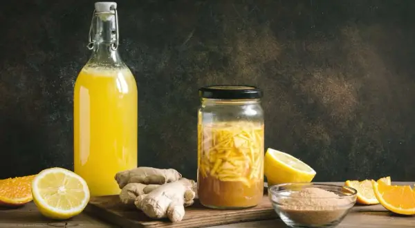 Zutaten für ingwer fermentieren: frischer Ingwer, Zitronen, Orangen und Zucker. Daneben eine Flasche mit gelbem Getränk.