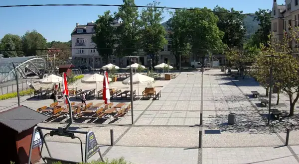 Letni dzień na rynku w Ustroniu. Puste stoliki kawiarniane czekają na gości, a słońce rzuca cienie na brukowany plac.