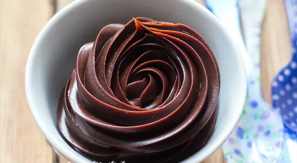 Una spirale perfetta di ganache cioccolato per copertura, lucida e invitante, in una ciotola bianca.