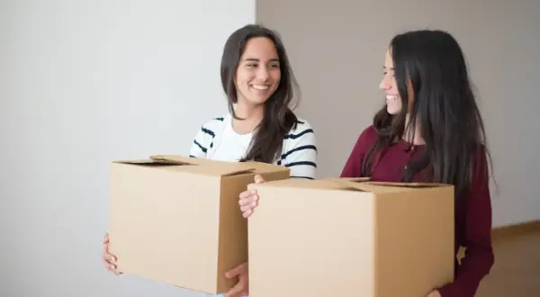 Due amiche sorridenti trasportano scatoloni, pronte per il precetto rilascio immobile prima della scadenza.