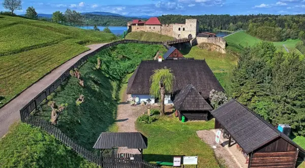 Widok z lotu ptaka na skansen z zamkiem, jeziorem i zielonymi wzgórzami.