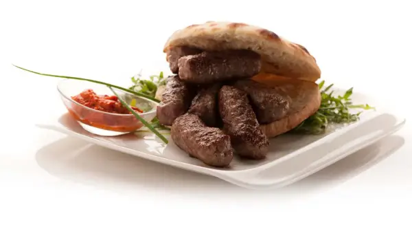 En tallrik med balkan mat: saftiga köttfärsrullar i pitabröd, serverade med en röd röra och grönsaker.