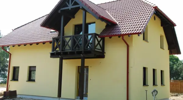 Jasnożółty dom z czerwonym dachem i drewnianym balkonem.