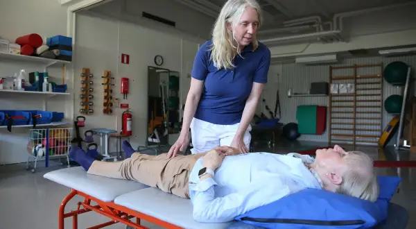 Fysioterapeut undersöker en patient som ligger på en brits. Patienten verkar vara fixerad bebis i sin position, redo för behandling.