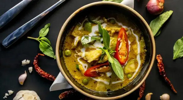 Aromatyczne curry z kurkumą, pełne zielonych warzyw i kawałków kurczaka, ozdobione chili i bazylią.
