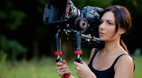 Kobieta trzymająca profesjonalną kamerę filmową na ramieniu.