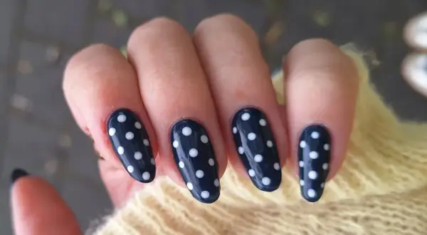 Manucure élégante avec un nail art pois sur fond bleu marine. Les ongles sont ornés de petits ronds blancs, créant un look ludique et chic.