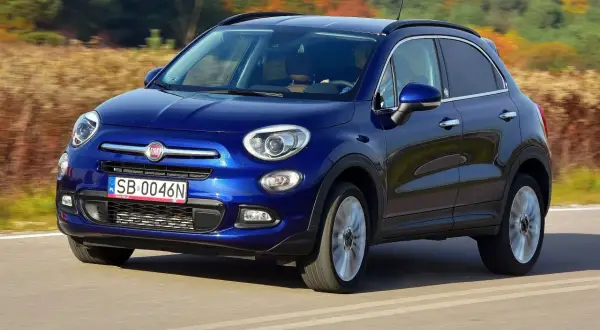 Błękitny Fiat 500X jedzie po drodze, otoczony jesienną przyrodą.