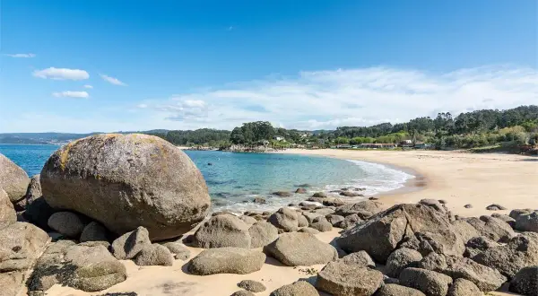 La **playa mourisca** se abre en una curva dorada bajo un cielo azul. Rocas gigantes y pequeñas salpican la arena y el agua turquesa.
