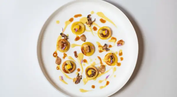 Piccolo capolavoro culinario: tartellette dorate con ripieno giallo, guarnite con calamari croccanti e fiori viola. Un'opera d'arte degna di un ristorante con massimo stelle Michelin.