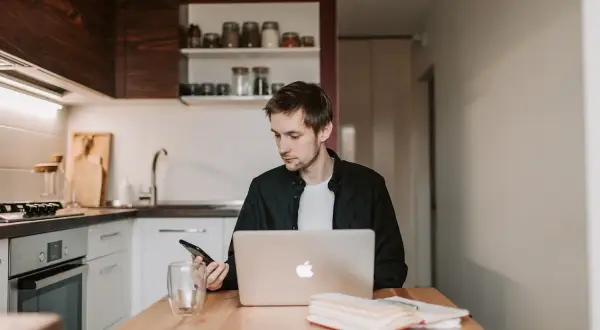 Mężczyzna w kuchni sprawdza telefon, bo Netia brak internetu uniemożliwia pracę na laptopie.