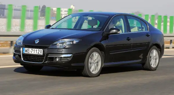 Czarny Renault Laguna 3 2.0 dCi jedzie po drodze, za zielonymi słupkami.
