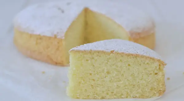 Una soffice torta con farina di riso, spolverata di zucchero a velo, con una fetta tagliata.