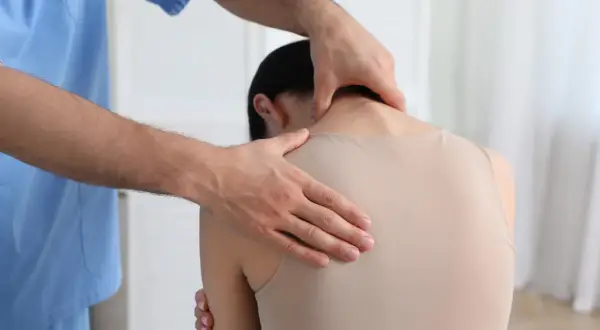 Fizjoterapeuta bada plecy pacjentki, szukając oznak garb na plecach.