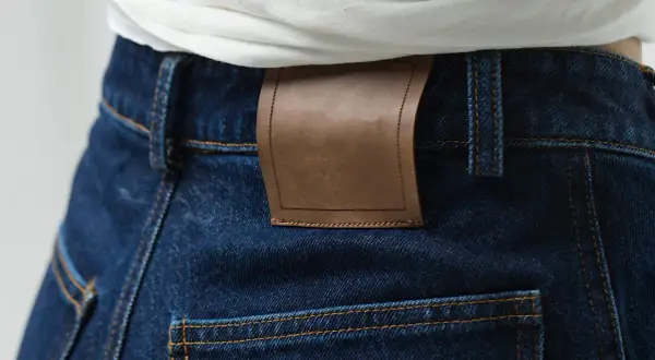 Detale ciemnych jeansów z brązową naszywką. Denim to materiał, z którego są wykonane.
