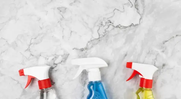 Tre flaconi spray su marmo bianco, pronti per scoprire come pulire il marmo macchiato.