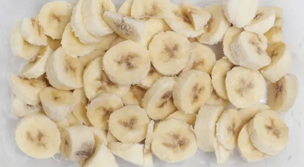 Pokrojone w plasterki banany w pojemniku, gotowe do mrożenia. To dowód, że banany można mrozić, idealne do smoothie!