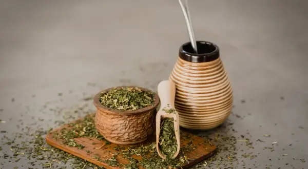 Naczynie z yerba mate i bombilla. Susz rozsypany na desce. Czy yerba mate ma właściwości negatywne?