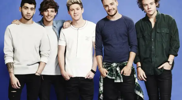 Pięciu członków One Direction pozuje do zdjęcia na niebieskim tle.