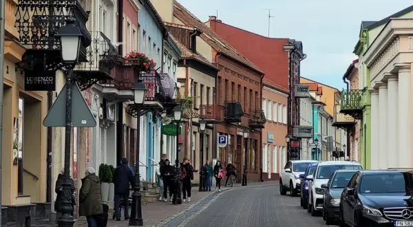 Urokliwa ulica w Koninie z kolorowymi kamieniczkami, balkonami i ludźmi spacerującymi po bruku. Odkryj **konin atrakcje** spacerując tymi uliczkami.