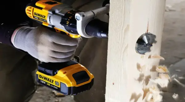 Ręka w rękawicy trzyma wiertarkę DeWalt, która wierci otwór w drewnie. Pokazano, jak włożyć wiertło do wiertarki.