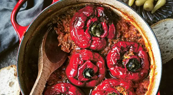 Röda, fyllda paprikor i en gryta med köttfärs och ris, redo att serveras med en träsked och en bit bröd.