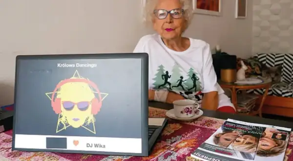 Starsza kobieta w okularach siedzi przy laptopie z grafiką DJ Wika.
