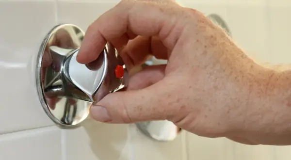 Hand dreht am Duschthermostat, um den wasseranschluss abzudichten.