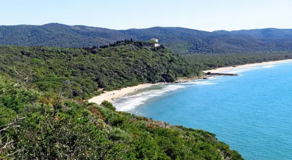 Spiaggia delle bandite di Scarlino, con mare azzurro, pineta lussureggiante e una villa in collina.