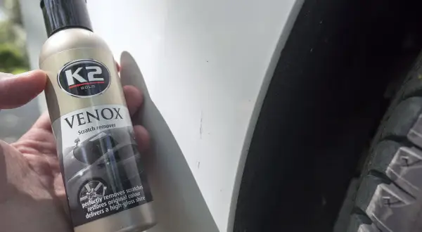 Jak usunąć rysy z samochodu domowym sposobem? Butelka K2 VENOX Scratch remover obok zarysowanego lakieru.