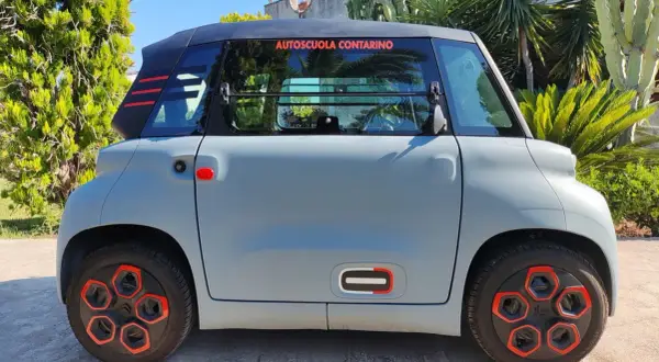 Citroën Ami grigia parcheggiata all'aperto, con dettagli rossi e neri. La scritta "Autoscuola Contarino" sul finestrino suggerisce un uso per l'apprendimento, con un'ottima **citroen ami autonomia** per la città.