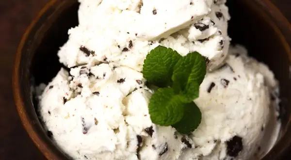 Cremiges Stracciatella Eis mit Schokoladenstückchen in einer Holzschale, garniert mit frischer Minze. Ein einfaches Stracciatella Eis Rezept zum Nachmachen.