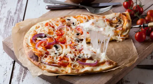 Rozciągający się ser z pizzy z pomidorami i cebulą na desce.