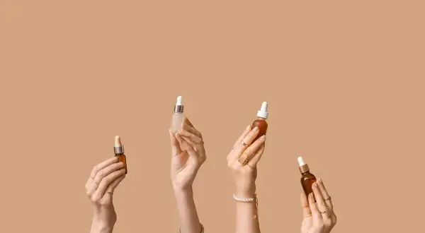 Cztery dłonie trzymają buteleczki z serum. Zastanawiasz się, kwas hialuronowy z czym łączyć?