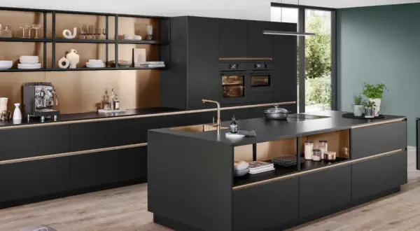 Cocina moderna con isla central, gabinetes negros, detalles dorados y electrodomésticos integrados.