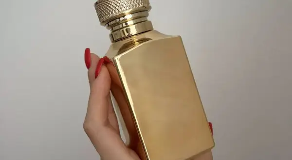 Złota butelka luksusowych perfum w dłoni z czerwonymi paznokciami. Elegancki flakon, który kusi zapachem.