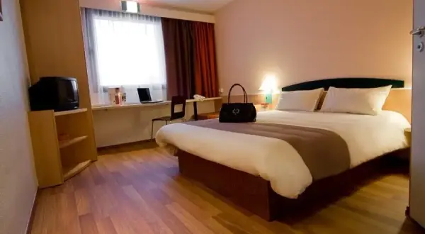 Pokój w Ibis Hotel Zabrze: łóżko, toaletka z laptopem, szafa z telewizorem i okno z zasłonami.