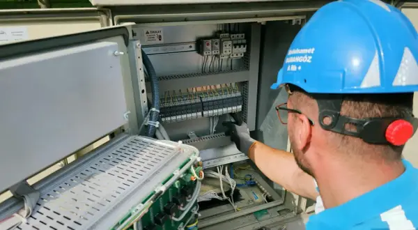 Elektryk w niebieskim kasku pracuje przy skrzynce elektrycznej. To oświadczenie o gotowości instalacji przyłączanej.