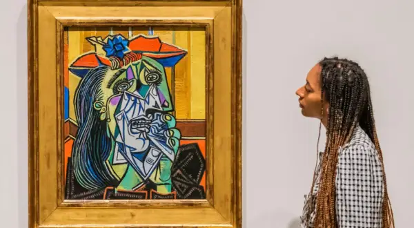 A woman gazes at a vibrant, cubist portrait, a striking example of obras de Pablo Picasso. The painting features a fragmented face with bold colors and sharp lines.